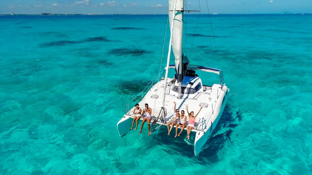 people waving hands seated in the security nets of nal gone catamaran while sailing over blue sea